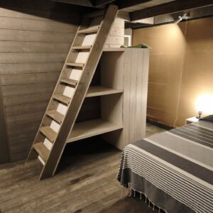 Interno del glamping dell’Amandolo con letto matrimoniale, pavimento e scala in legno